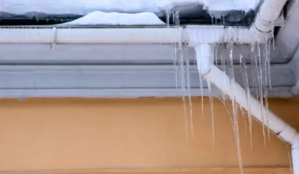 Ice-covered gutter and rain spout requiring winter gutter maintenance to prevent ice dams and water damage.