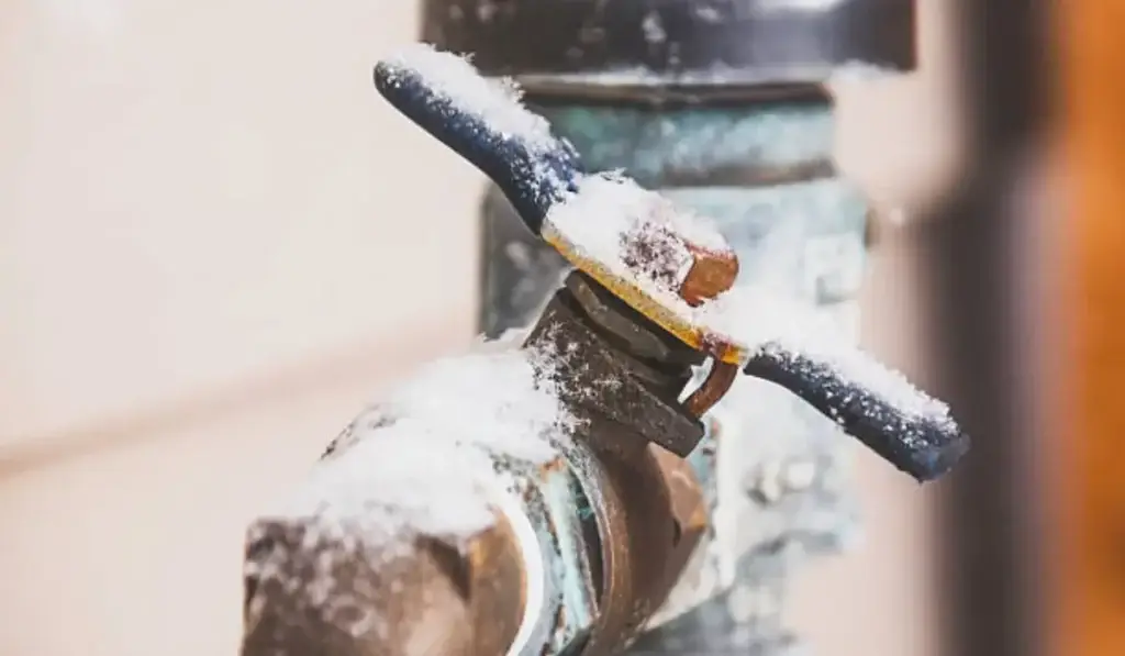 Close-up of outdoor faucet covered in ice, showing frozen pipes that can cause plumbing damage in winter.
