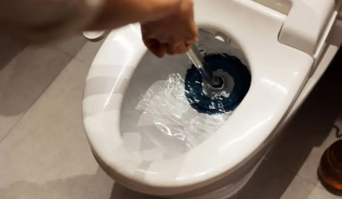 Person using a plunger in a clogged toilet with blue cleaning solution, attempting to clear the blockage.