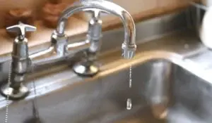 Close-up of leaky faucets dripping water into a stainless steel sink in Naperville, IL.