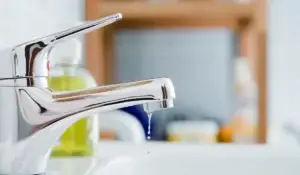 leaky faucet dripping water in bright bathroom sink.