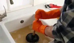 Slow drainage in a kitchen sink being fixed with a plunger.
