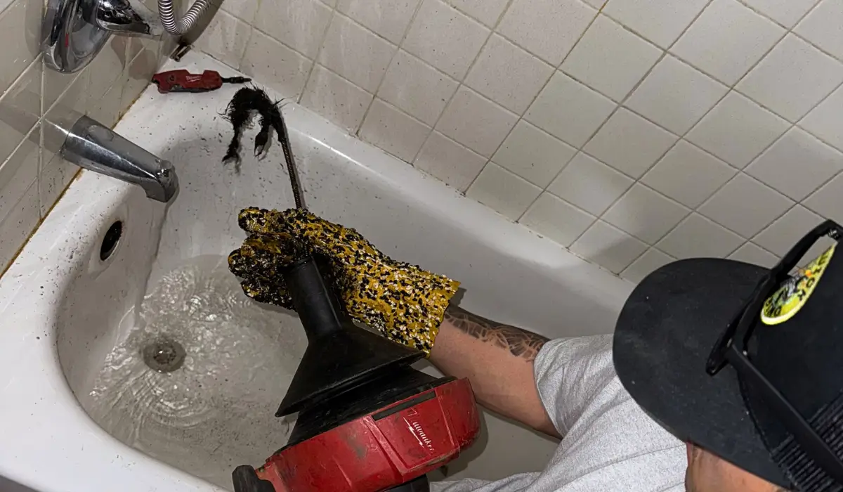 Plumber using a power auger to clear a clogged bathtub drain causing a gurgling sound.
