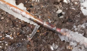 A frozen copper pipe leaking water outdoors, emphasizing the need to prepare your plumbing in Naperville IL before severe winter temperatures cause damage.